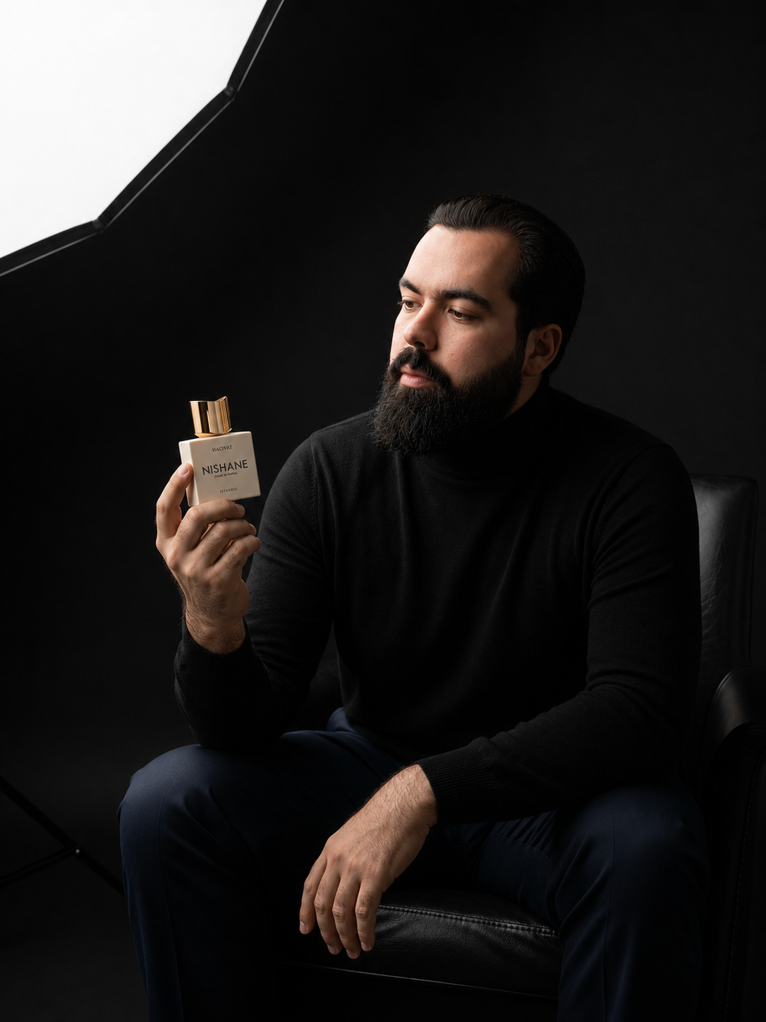 Rafael segurando um perfume premium em estúdio escuro